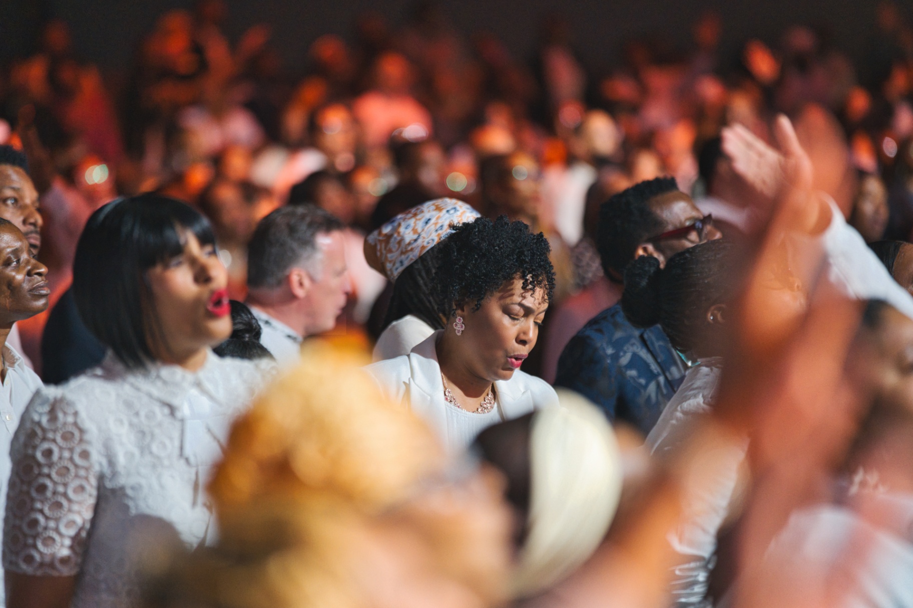 Crowd in white worshipping under warm stage light
